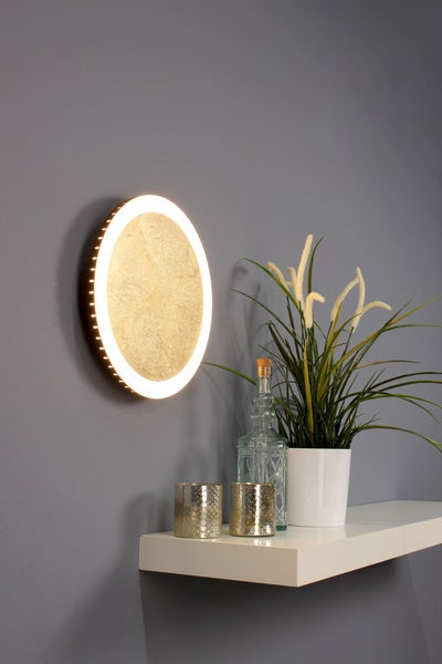 Runde Wandleuchte mit goldfarbenem strukturiertem Zentrum und LED-Lichtring, montiert über einem Regal mit Dekoration.