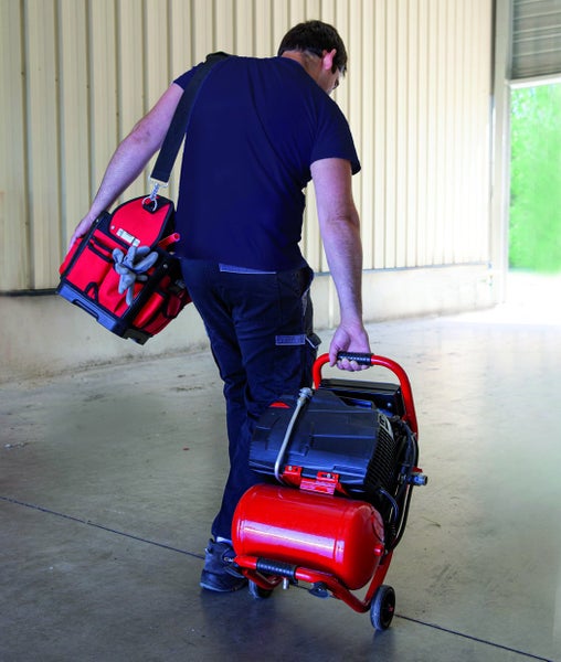 Eine Person trägt einen Kompressor, eine Werkzeugtasche und Handschuhe.