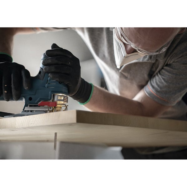 Eine Person arbeitet mit einer Stichsäge an einem Werkstück. Sie trägt dabei Handschuhe, eine Schutzbrille und einen Mundschutz.