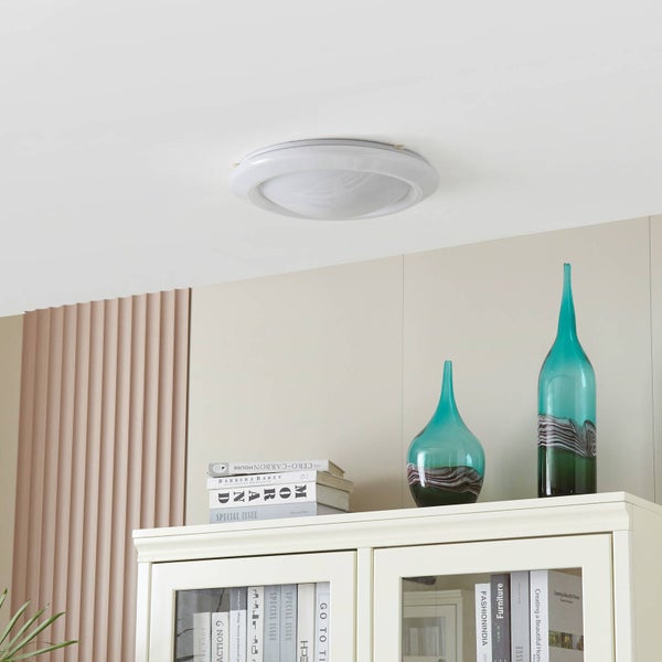 Runde weiße Deckenleuchte an einer Zimmerdecke in einem hellen Wohnraum über einem weißen Glasschrank mit Dekoration.