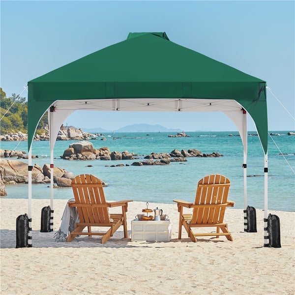 Szene mit grünem Faltpavillon, zwei Holzstühlen und schwarzen Sandsäcken am Strand