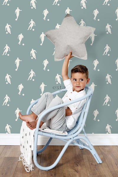 Dekoratives Kinderzimmer mit Fußballtapete, Sternkissen und blauem Rattan-Schaukelstuhl.