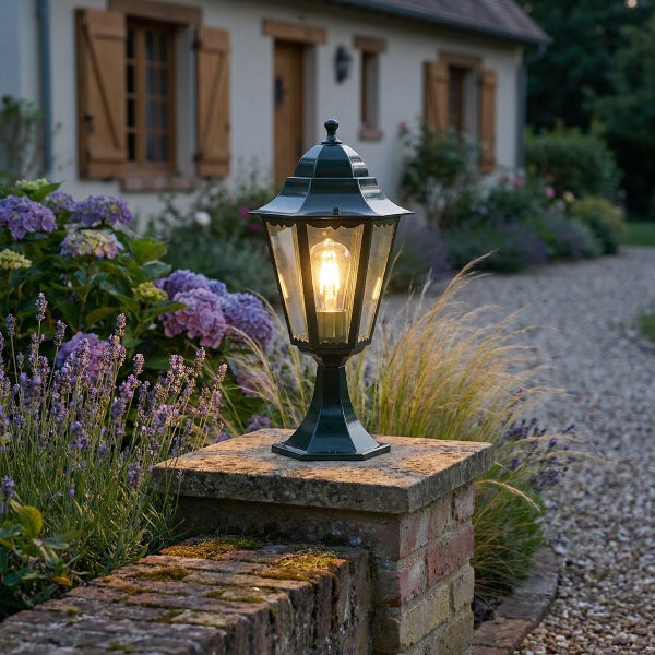 Klassische Außen-Sockelleuchte aus Metall und Glas, montiert auf einem Steinpfeiler in einem Garten mit Blumen und Kiesweg.