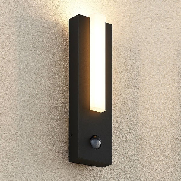 Schwarze LED Außenwandleuchte mit Bewegungsmelder und rechteckigem Lichtelement leuchtet warmweiß an einer Wand.