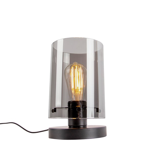 Industrielle Tischleuchte mit rauchfarbenem Glaszylinder und schwarzem Metallfuß, inklusive sichtbarem Filament-Leuchtmittel.