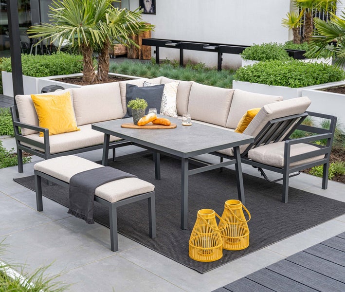 Moderne Garten Lounge Gruppe mit Ecksofa, Esstisch und Sitzbank auf einer Terrasse, Metallgestell mit hellen Polstern und Zierkissen.