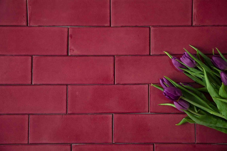 Dunkelrote Wandfliesen in Ziegeloptik, rechteckig mit glänzender Oberfläche, dekorative Tulpen an der Seite.