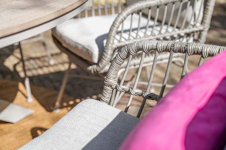 Nahaufnahme eines Gartenstuhls aus grauem Geflecht mit Sitzkissen auf einer Terrasse.