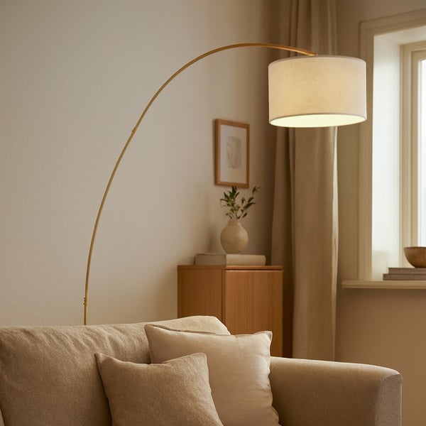 Goldfarbene Bogenstehleuchte mit hellem Textilschirm hinter einem beigen Sofa in einem hellen, modern eingerichteten Wohnzimmer.