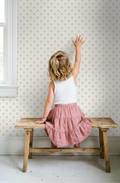 Ein heller Raum mit Tapete in einem kleinen floralen Gittermuster. Ein Kind sitzt auf einer Holzbank und greift nach der gemusterten Wand.
