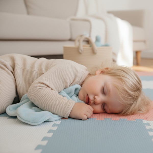 Ein Kleinkind schläft friedlich auf einer gepolsterten Spielmatte im Wohnzimmer, neben einem Aufbewahrungskorb und einem Sofa.