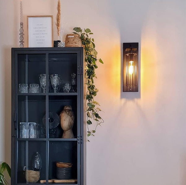 Innenaufnahme eines Wohnzimmers mit einem dunklen Vitrinenschrank, einer Zimmerpflanze und einer Wandleuchte