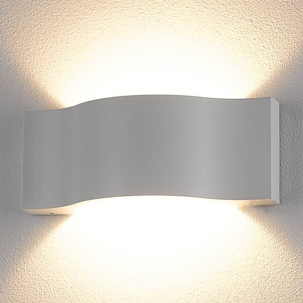 Moderne Wandleuchte in Wellenform mit Lichtaustritt nach oben und unten an einer strukturierten Wand.