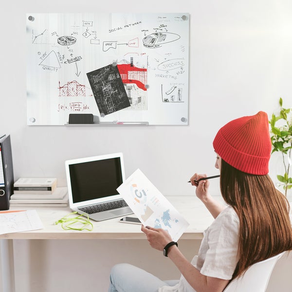 Magnetische Glas-Magnetwand in einem hellen Büro über einem Schreibtisch mit Laptop und einer arbeitenden Person.