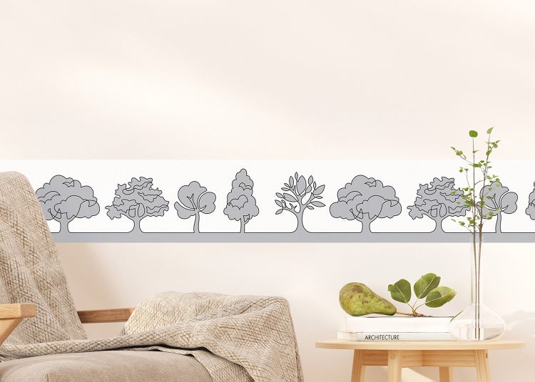 Tapetenbordüre mit Baummotiv an einer Wand in einem hellen, organisierten Raum mit Sessel und Beistelltisch.