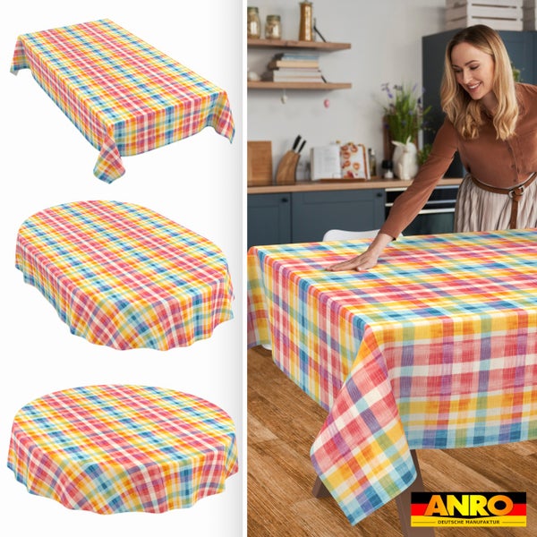 Bunt karierte Wachstuch-Tischdecke in rechteckiger, ovaler und runder Form. Frau glättet das Tuch am Esstisch. ANRO Deutsche Manufaktur Logo.