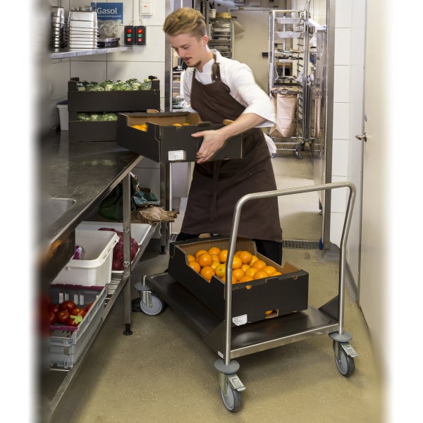 Person in einer Profiküche hebt einen Karton mit Orangen von einem Plattformwagen aus Edelstahl auf eine Arbeitsfläche. Der Wagen hat vier Rollen.