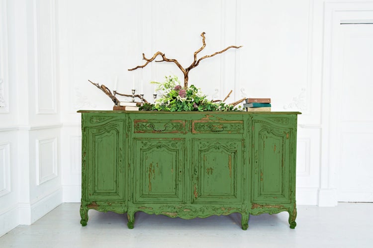 Grüner Holzschrank im Landhausstil mit Schubladen und Türen, dekoriert mit Blumen, Ästen und Büchern.