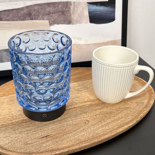 Blaues Glaswindlicht mit Teelichthalter und weißer Tasse auf einem Holztablett