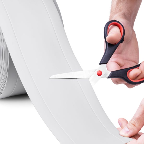 Zuschneiden einer grauen, flexiblen Weichsockelleiste von der Rolle mit einer Schere.