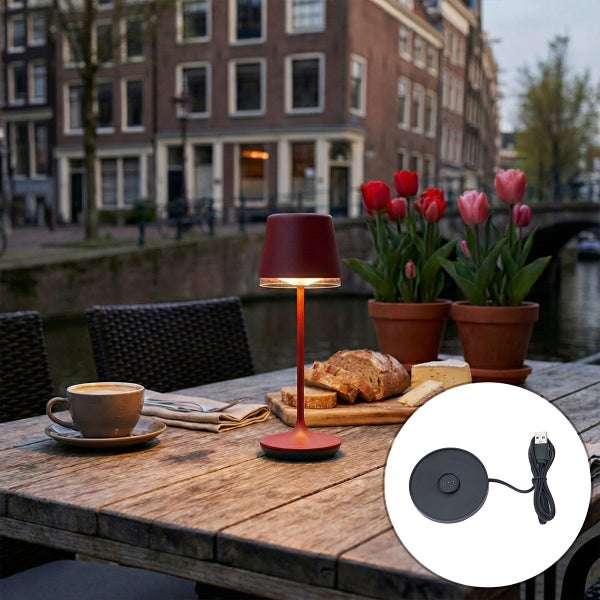 Akkubetriebene LED-Tischleuchte für den Außenbereich auf einem Holztisch mit Brot, Käse und Tulpen, inklusive USB-Ladestation.