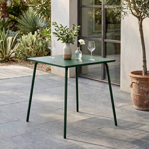 Quadratischer dunkelgrüner Metall-Gartentisch auf einer Steinterrasse mit dekorativen Vasen und Gläsern, mediterraner Gartenstil.