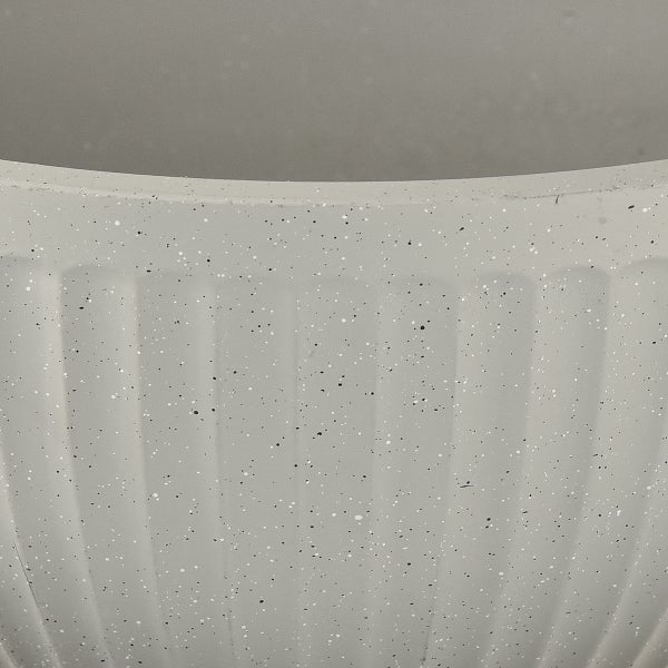 Nahaufnahme eines Pflanztopfes mit gesprenkelter Oberfläche und vertikaler Riffelung in Steinoptik.