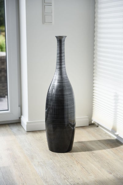 Große Bodenvase mit schmalem Hals und horizontaler Struktur auf hellem Bodenbelag in einem hellen Raum.