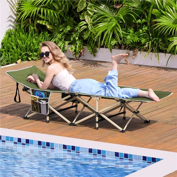 Frau liegt auf einer grünen Sonnenliege mit Taschen auf einer Holzterrasse neben einem Schwimmbecken.