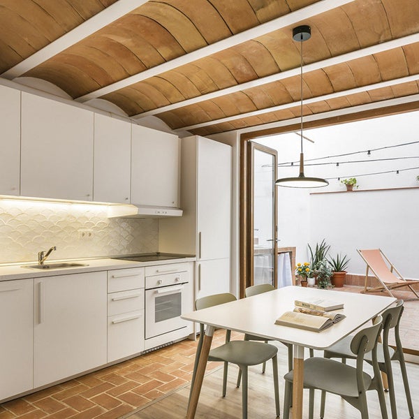 Moderne Küche mit weißen Einbauschränken und gewölbter Ziegeldecke angrenzend an eine Terrasse mit Außenbereich.