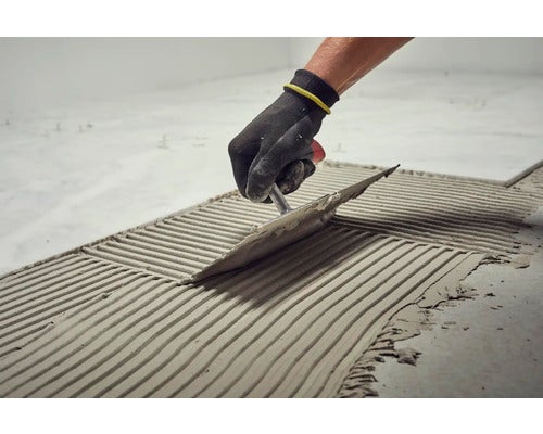 Fliesenleger trägt Fliesenkleber mit einer Glättkelle auf den Boden auf.