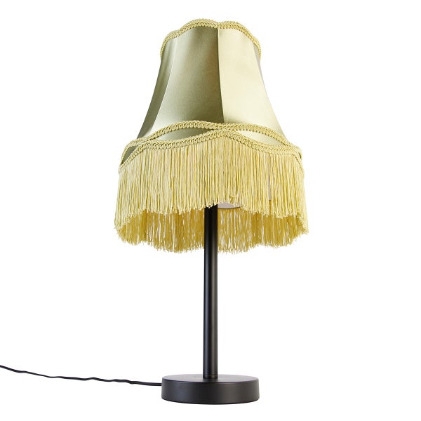 Tischleuchte mit schwarzem Metallfuß und Stoffschirm mit Fransen sowie dekorativer Borte.