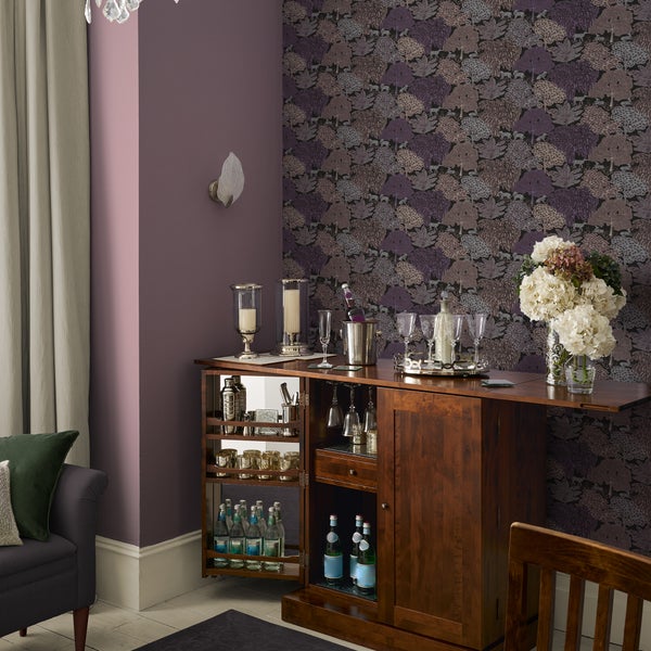 Einrichtung einer Hausbar mit einer dunklen Holzbar, geschmückt mit Glaswaren, Dekoration und einem floralen Wandmuster in einem eleganten Wohnzimmer.