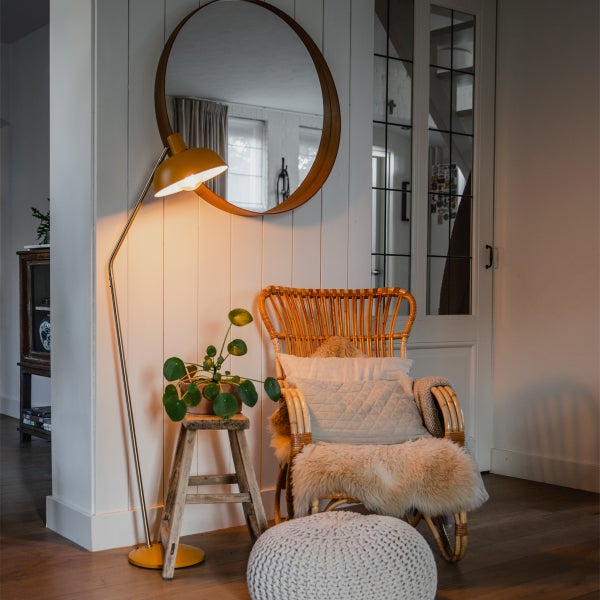 Wohnzimmer-Szene mit Stehlampe, Rattansessel, Spiegel und Dekoration für eine gemütliche Atmosphäre