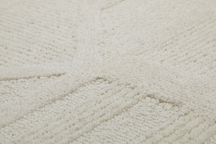 Beige zusammengerollter Teppich mit Reliefstruktur und unterschiedlichen Florhöhen.