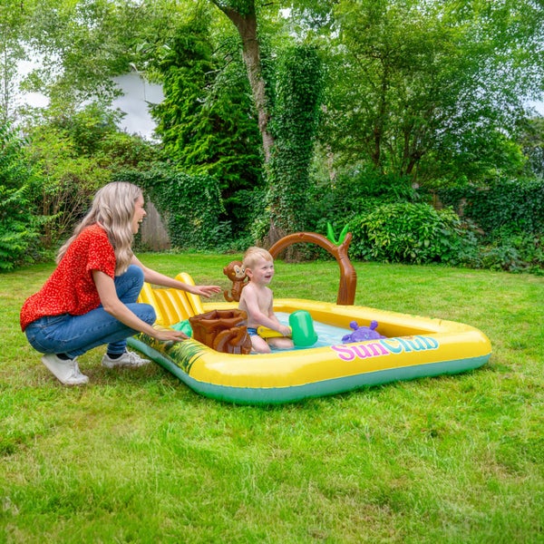 Eine Frau spielt mit einem kleinen Kind in einem aufblasbaren Dschungel Spielcenter Planschbecken von SunClub im Garten.