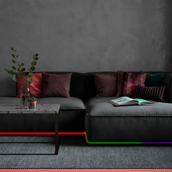 Modernes Wohnzimmer mit farbiger LED-Streifen-Beleuchtung unter einem dunkelgrauen Sofa, Marmor-Couchtisch und dekorativen Kissen.