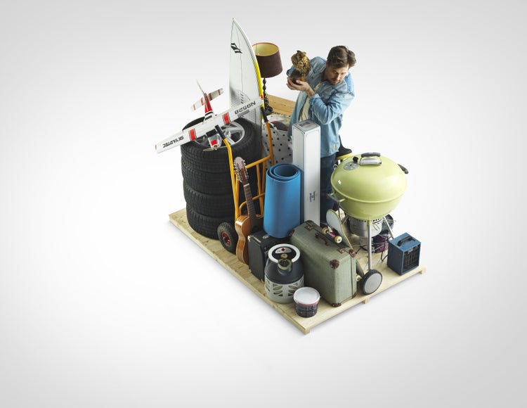 Mann steht auf einer Holzpalette mit verschiedenen Haushalts- und Freizeitartikeln wie Grill, Reifen, Koffer, Gitarre und Surfbrett.
