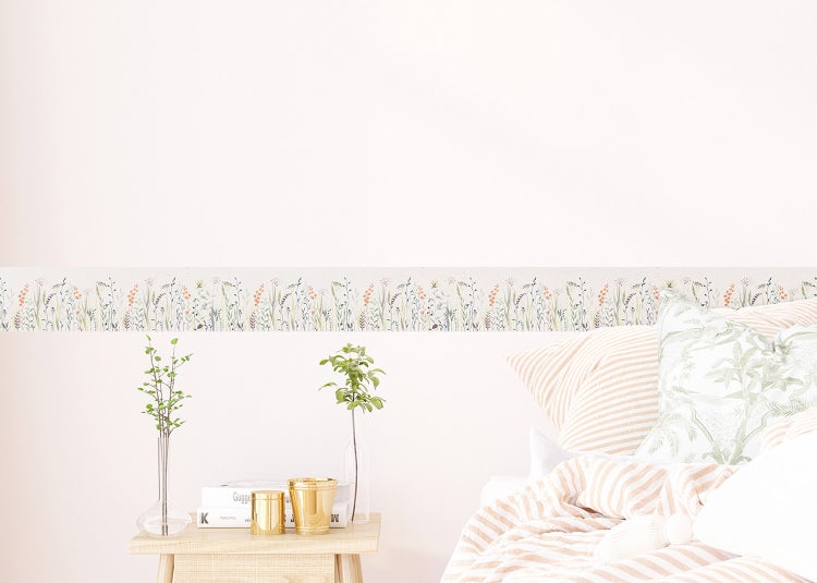 Tapetenbordüre mit floralem Muster in Aquarell-Optik an einer Wand in einem hellen Raum mit Tisch und Stuhl.
