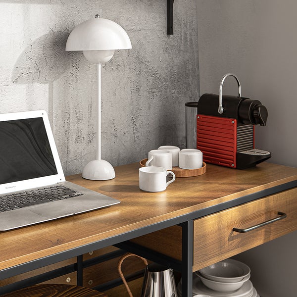 Arbeitsbereich mit Laptop, Lampe, Kaffeemaschine und Tassen auf einem Schreibtisch.