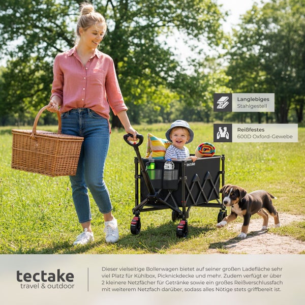 Frau zieht Bollerwagen mit Kind und Hund durch Park. Im Bollerwagen befinden sich Getränke und eine Picknickdecke. Die Frau trägt einen Picknickkorb.