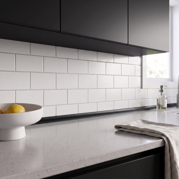 Moderne Küche mit hellen Wandfliesen im Ziegelverbund, dunklen Oberschränken und einer Arbeitsplatte mit Sprenkelmuster sowie Geschirrtuch und Obst.