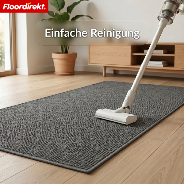 Floordirekt Logo. Strukturierter grauer Teppich auf hellem Holzfußboden wird mit einem Staubsauger gereinigt. Text: Einfache Reinigung.