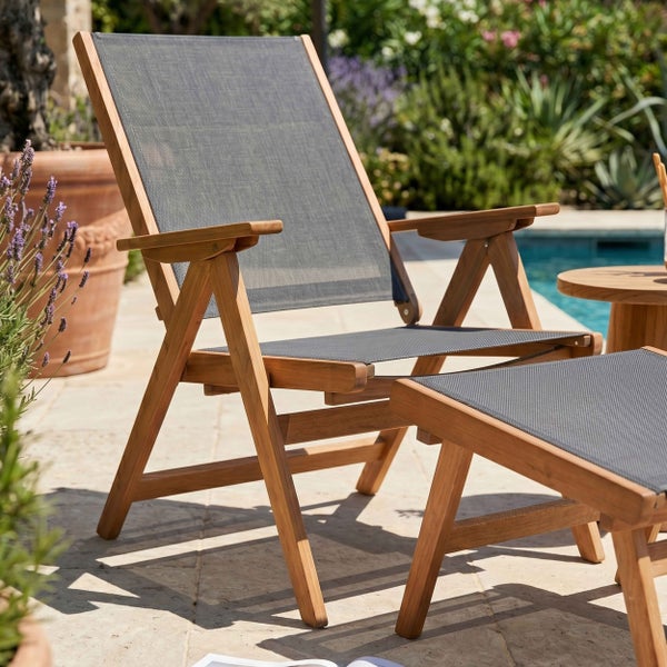 Gartenstuhl und Hocker aus Holz mit Textilbespannung auf einer hellen Terrasse neben einem Pool.
