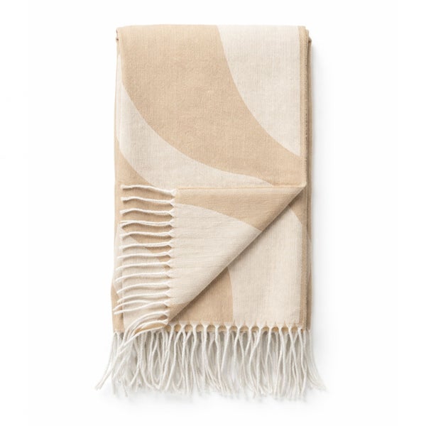 Gefaltete Wohndecke mit beige-weißem Wellenmuster und weißen Fransen.