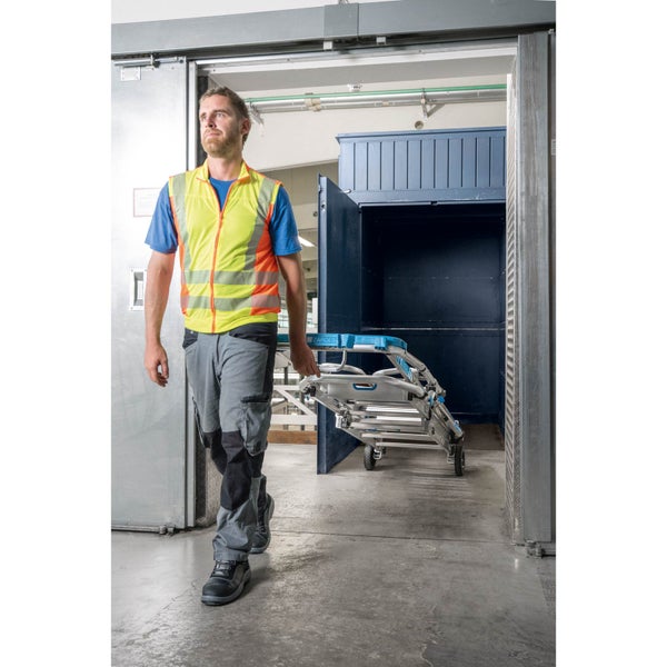 Eine Person mit Sicherheitsweste trägt eine Zarges Treppenkarre durch einen Durchgang.