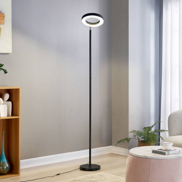 Moderne LED-Stehleuchte mit ringförmigem Leuchtkopf in einem hellen Wohnzimmer mit Bücherregal, Beistelltisch und Zimmerpflanze.