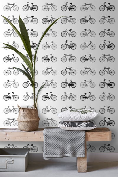 Dekorative Szene mit einer Pflanze in einem Korb, Kissen und einer Decke auf einer Holzbank vor einer Tapete mit Fahrradmuster.