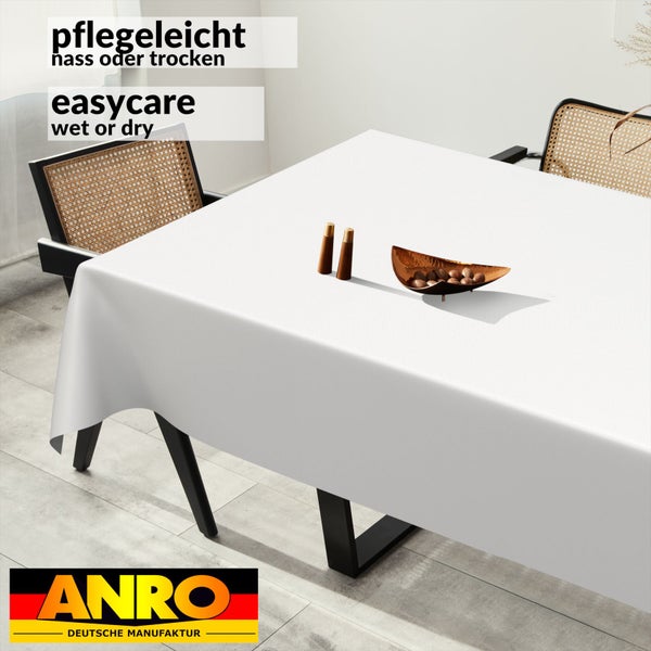Weiße, nass oder trocken pflegeleichte Tischdecke auf einem Esstisch mit Rattan-Stühlen, Salz- und Pfefferstreuern und einer Schale. ANRO Logo.