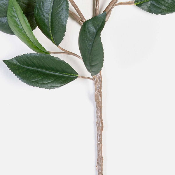 Nahaufnahme eines künstlichen Zweigs mit dunkelgrünen gezackten Blättern und einem braunen strukturierten Stiel.